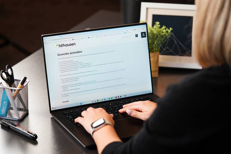 Eine weibliche Person sitzt an einem Schreibtisch vor einem Laptop.